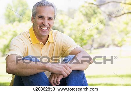 Stock Image - Man sitting outdoors smiling. Fotosearch