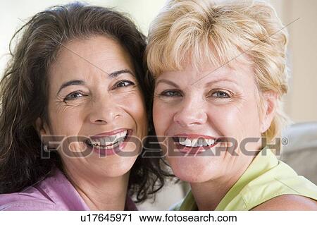 Stock Image - Two women in living room smiling. Fotosearch