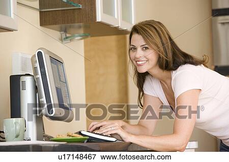 Stock Photo - Woman in kitchen with computer smiling. Fotosearch