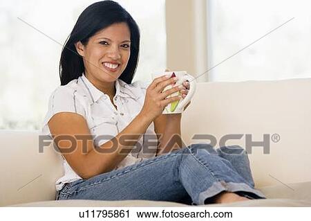 Stock Image - Woman in living room with coffee smiling. Fotosearch