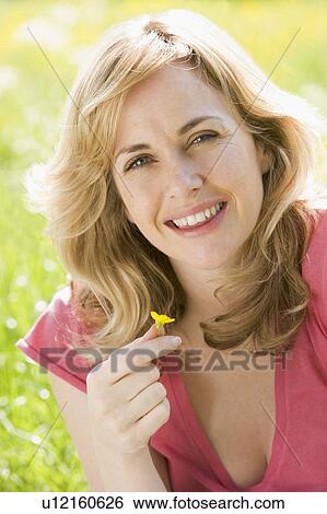 Stock Photograph - Woman sitting outdoors holding flower smiling. Fotosearch