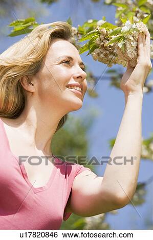 Stock Photograph - Woman standing outdoors holding blossom smiling. Fotosearch