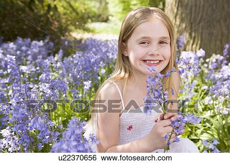 Stock Photograph - Young girl outdoors holding flowers smiling. Fotosearch
