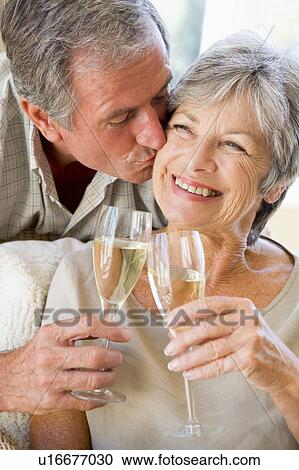 Stock Image - Couple in living room toasting champagne kissing and smiling. Fotosearch