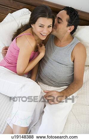Stock Photo - Couple relaxing on bed in bedroom snuggling and smiling (selective focus). Fotosearch