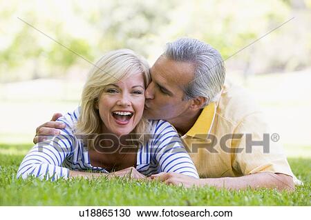 Stock Image - Couple relaxing outdoors in park kissing and smiling. Fotosearch