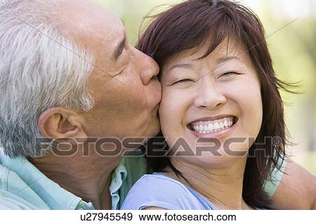 Couple relaxing outdoors in park kissing and smiling View Large Photo Image Stock Photo - Couple relaxing outdoors in park kissing and smiling. Fotosearch