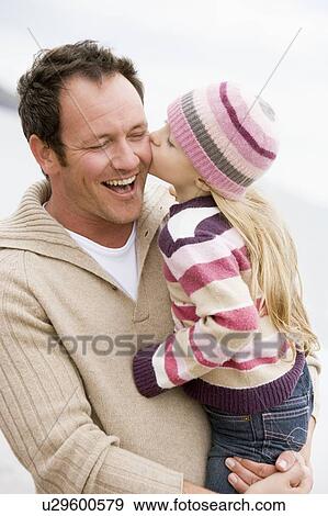 Stock Photo - Father holding daughter kissing him at beach smiling. Fotosearch