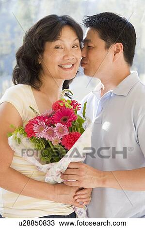 Husband and wife holding flowers kissing and smiling View Large Photo Image Stock Image - Husband and wife holding flowers kissing and smiling. Fotosearch