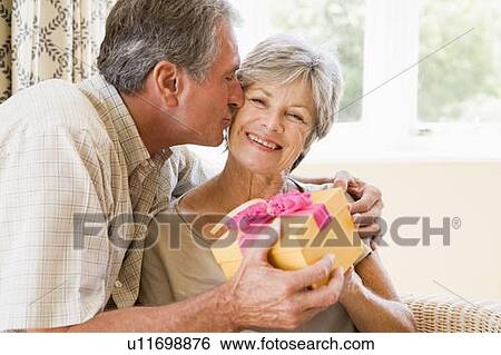 Stock Photograph - Husband giving wife gift in living room kissing her and smiling. Fotosearch