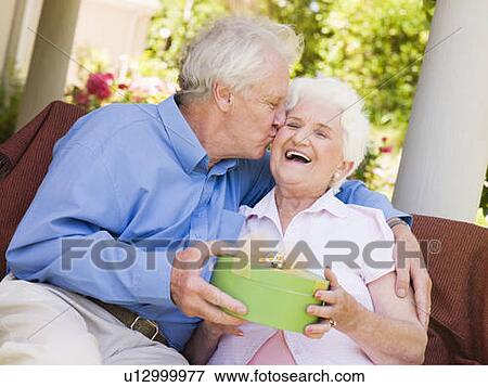 Husband giving wife gift on patio kissing her and smiling View Large Photo Image Stock Photo - Husband giving wife gift on patio kissing her and smiling. Fotosearch