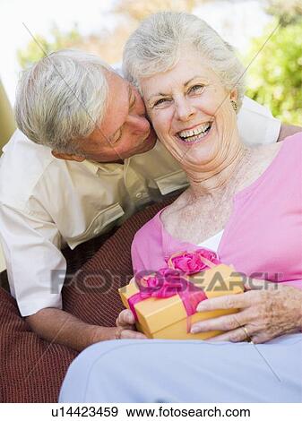 Stock Photo - Husband giving wife gift on patio kissing her and smiling. Fotosearch