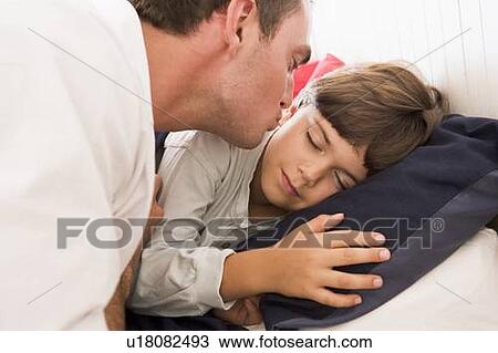 Stock Image - Man waking young boy in bed with kiss. Fotosearch
