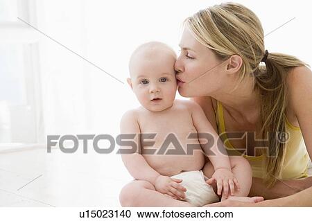 Stock Image - Mother kissing baby indoors. Fotosearch