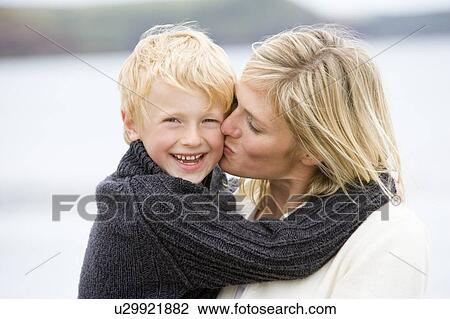 Stock Image - Mother kissing son at beach smiling. Fotosearch
