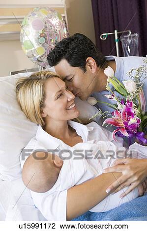 Stock Image - New mother with baby and husband in hospital smiling. Fotosearch