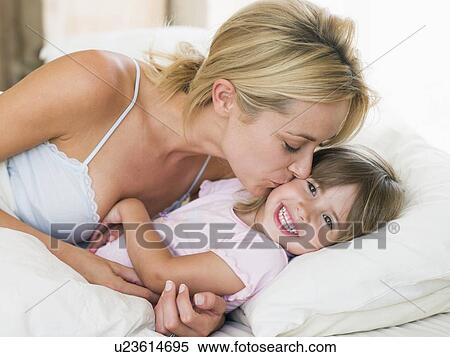 Stock Photography - Woman kissing young girl in bed smiling. Fotosearch