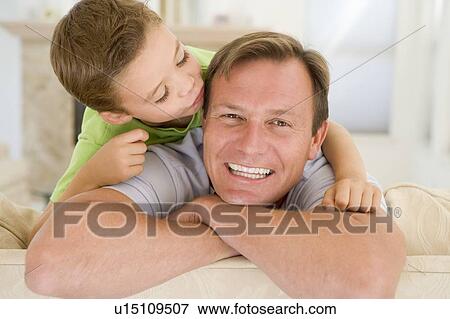Stock Photo - Young boy kissing smiling man in living room. Fotosearch