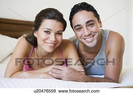 Couple relaxing on bed in bedroom smiling (selective focus) View Large Photo Image Stock Photo - Couple relaxing on bed in bedroom smiling (selective focus). Fotosearch