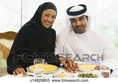 Stock Image - Couple sitting at dinner table smiling (high key). Fotosearch