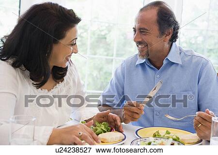Stock Photo - Couple sitting at dinner table smiling (high key). Fotosearch