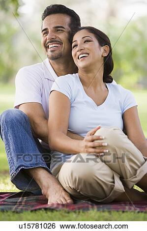 Couple sitting outdoors in park smiling (selective focus) View Large Photo Image Stock Photograph - Couple sitting outdoors in park smiling (selective focus). Fotosearch
