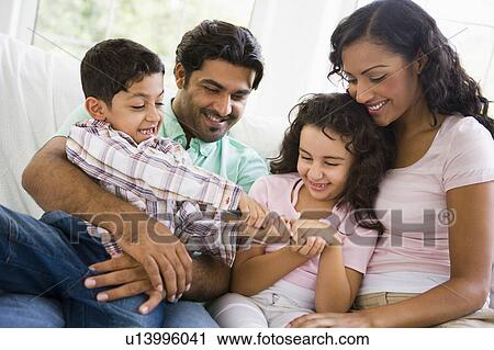 Stock Image - Family in living room fighting over remote control smiling (high key). Fotosearch