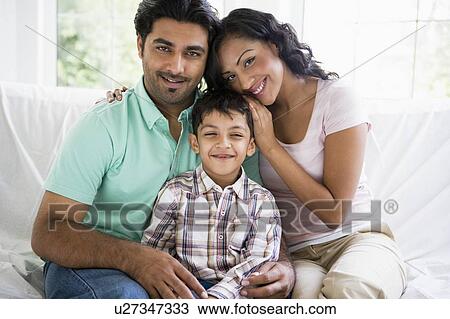 Stock Image - Family in living room sitting on sofa smiling (high key). Fotosearch
