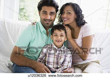 Stock Photograph - Family in living room sitting on sofa smiling (high key). Fotosearch