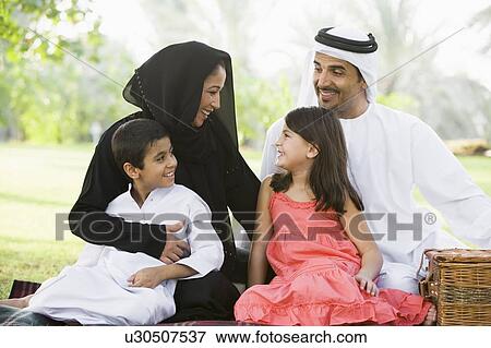 Stock Photo - Family outdoors in park having a picnic and smiling (selective focus). Fotosearch