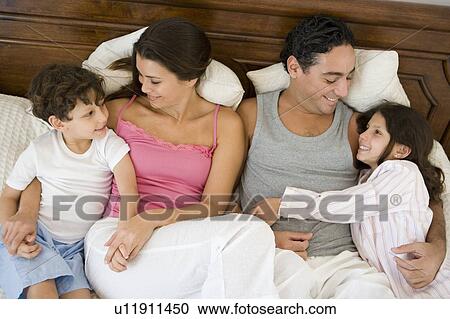 Stock Image - Family relaxing on bed in bedroom smiling (selective focus). Fotosearch