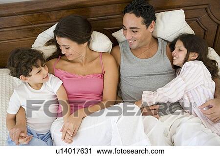 Stock Image - Family relaxing on bed in bedroom smiling (selective focus). Fotosearch