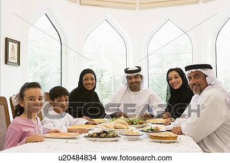 Picture - Family sitting at dinner table smiling (high key). Fotosearch