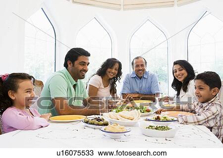 Family sitting at dinner table smiling (high key) View Large Photo Image Stock Image - Family sitting at dinner table smiling (high key). Fotosearch