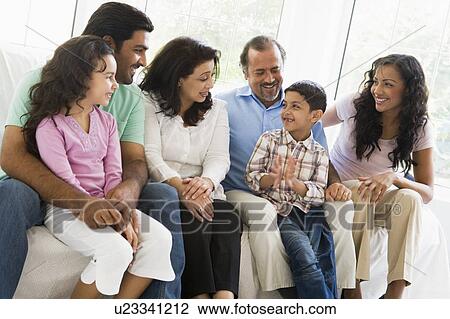 Stock Image - Family sitting in living room smiling (high key). Fotosearch