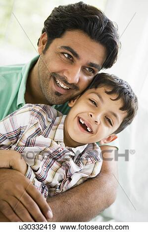 Stock Photo - Father and son in living room smiling (high key). Fotosearch