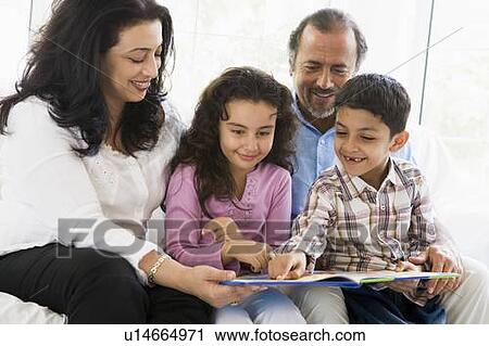 Stock Image - Grandparents sitting in living room reading with grandchildren smiling (high key). Fotosearch