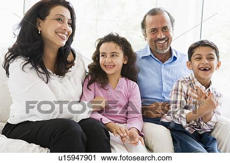 Stock Image - Grandparents sitting in living room with grandchildren smiling (high key). Fotosearch