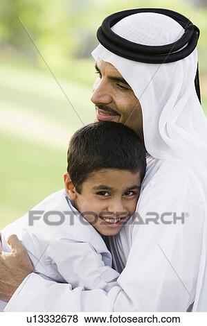 Stock Photo - Man and young boy outdoors in park embracing and smiling (selective focus). Fotosearch