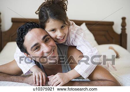Stock Image - Man and young girl relaxing on bed in bedroom smiling (selective focus). Fotosearch