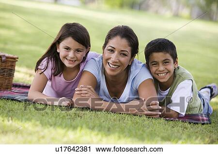 Stock Image - Mother and two young children outdoors in park with picnic smiling (selective focus). Fotosearch