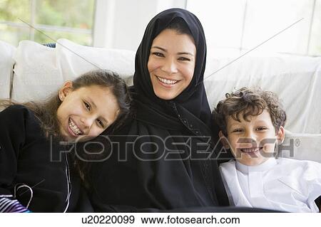 Stock Photo - Mother and two young children sitting in living room smiling (high key/selective focus). Fotosearch