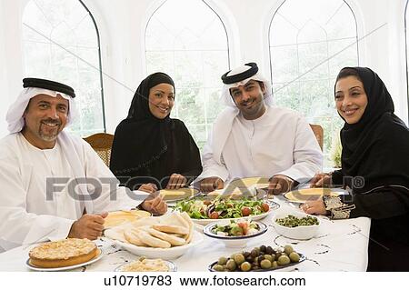 Stock Image - Two couples sitting at dinner table smiling (high key). Fotosearch