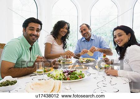 Stock Image - Two couples sitting at dinner table smiling (high key). Fotosearch