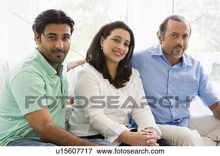 Stock Photo - Two men and a woman sitting in living room smiling (high key). Fotosearch