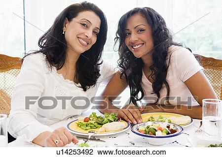 Two women sitting at dinner table smiling (high key) View Large Photo Image Stock Image - Two women sitting at dinner table smiling (high key). Fotosearch