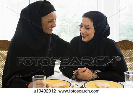 Two women sitting at dinner table smiling (high key) View Large Photo Image Stock Image - Two women sitting at dinner table smiling (high key). Fotosearch