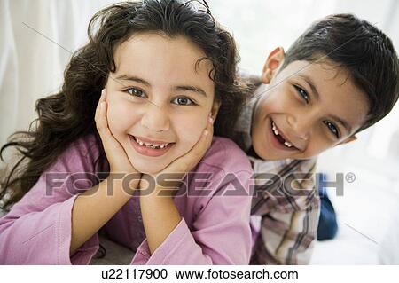 Stock Image - Two young children playing in living room smiling (high key). Fotosearch