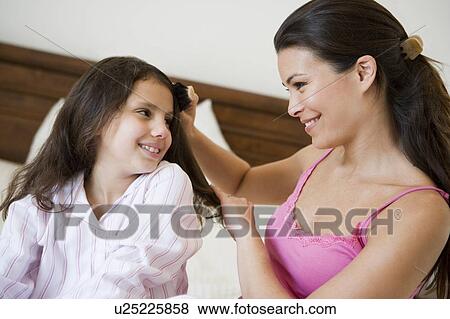 Woman brushing young girl's hair on bed in bedroom smiling (selective focus) View Large Photo Image Stock Photo - Woman brushing young girl's hair on bed in bedroom smiling (selective focus). Fotosearch