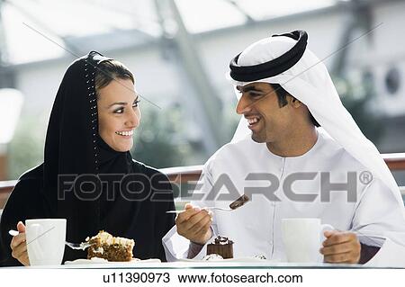 Stock Image - Couple at restaurant eating dessert and smiling (selective focus). Fotosearch